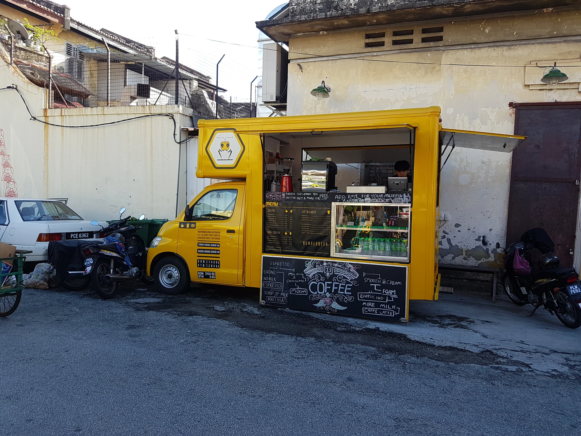 Bright yellow coffee truck against a weathered wall in George Town, Penang