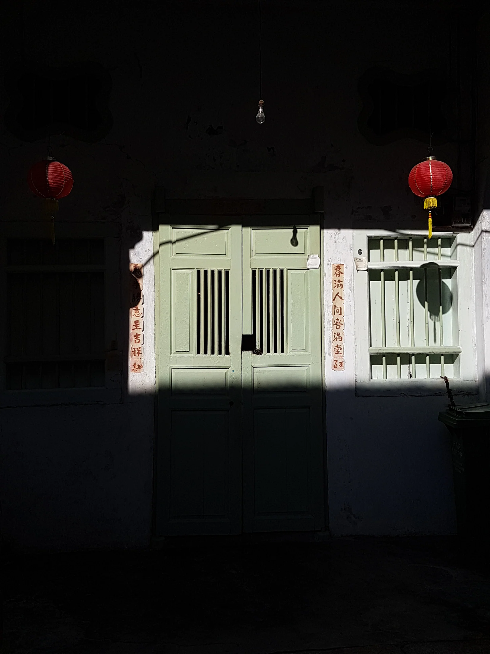 Green heritage doorway and red lanterns in sharp afternoon light in George Town, Penang